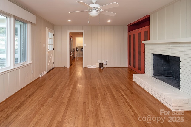 unfurnished living room with visible vents, a brick fireplace, light wood-style flooring, and washer and clothes dryer