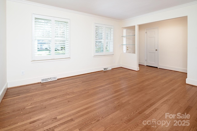 empty room with visible vents, ornamental molding, baseboards, and wood finished floors