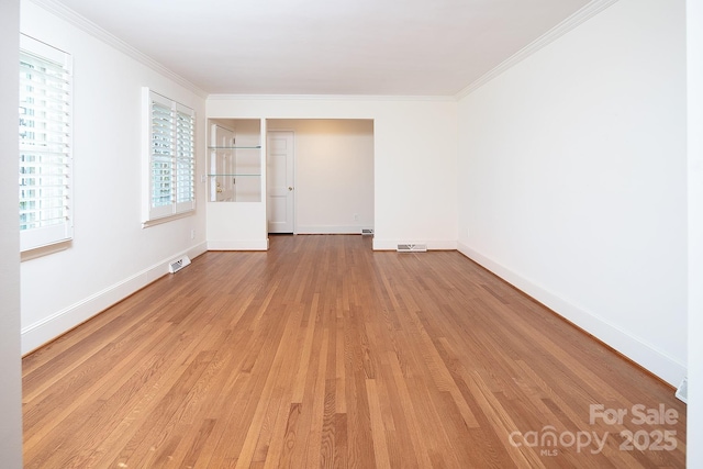 empty room featuring crown molding, light wood-style floors, visible vents, and baseboards