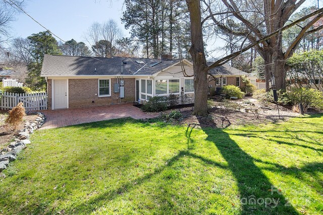 rear view of property with a patio area, a yard, brick siding, and fence