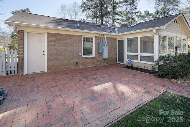 rear view of property with brick siding, a shingled roof, a chimney, a sunroom, and a patio area