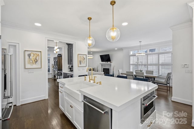 kitchen featuring dark wood finished floors, a fireplace, crown molding, stainless steel appliances, and a sink