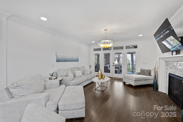 living area featuring dark wood-style floors, french doors, crown molding, a tiled fireplace, and an inviting chandelier