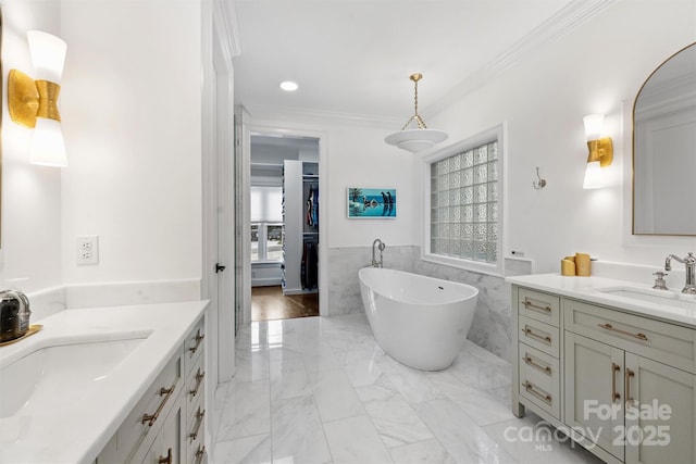 full bath featuring marble finish floor, ornamental molding, a freestanding tub, and a sink