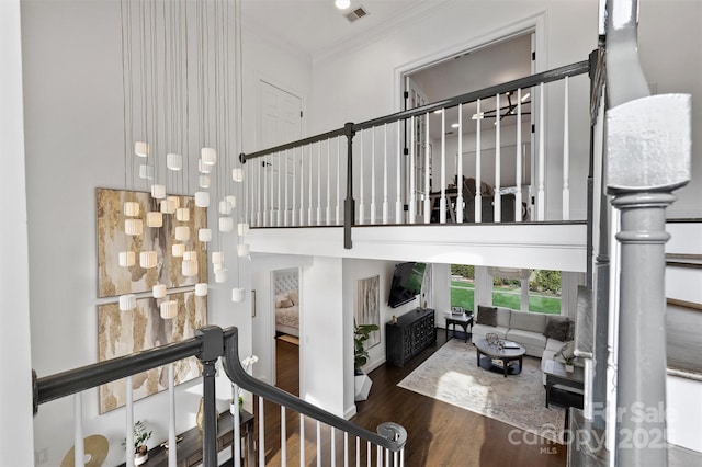 stairs with a high ceiling, visible vents, wood finished floors, and ornamental molding