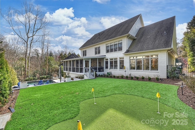 rear view of house featuring an outdoor pool, a lawn, a patio, a sunroom, and brick siding