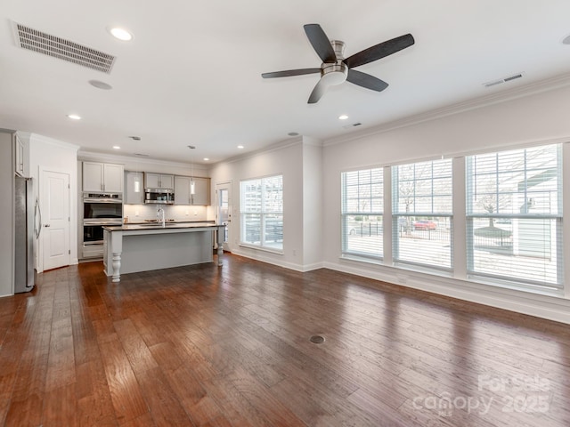 unfurnished living room with crown molding, visible vents, dark wood-type flooring, and a sink