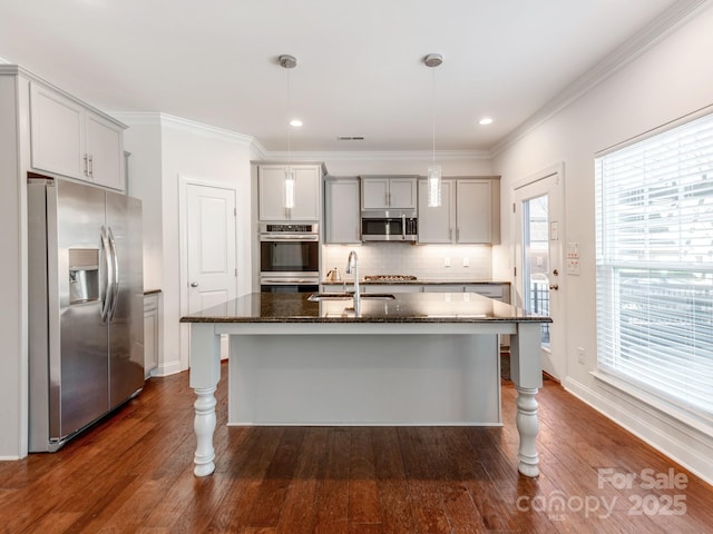 kitchen with tasteful backsplash, appliances with stainless steel finishes, dark wood-type flooring, a sink, and dark stone counters