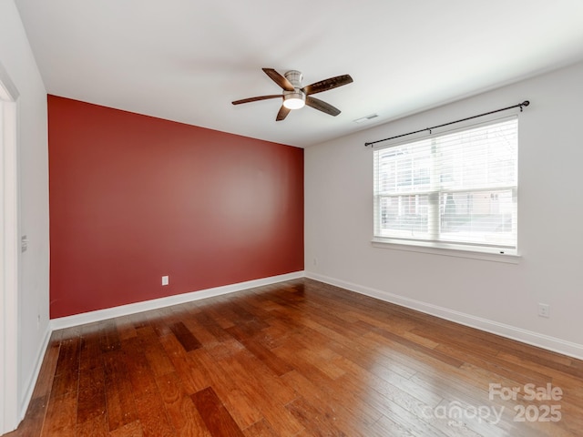 spare room featuring a ceiling fan, wood finished floors, visible vents, and baseboards