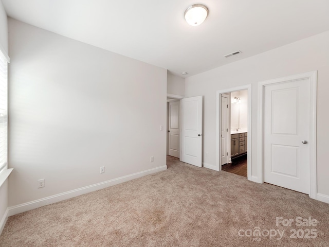 unfurnished bedroom featuring ensuite bath, baseboards, visible vents, and carpet flooring