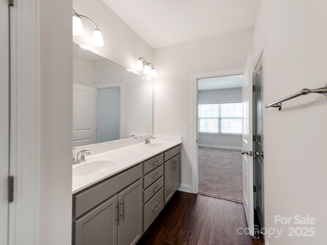 full bath featuring double vanity, baseboards, a sink, and wood finished floors