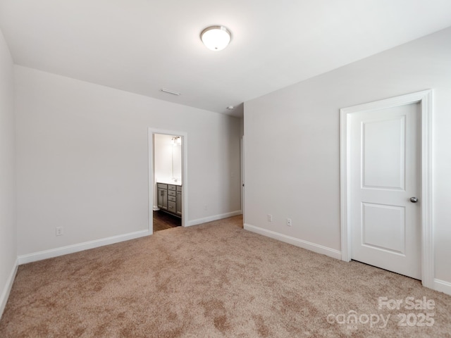 unfurnished bedroom with ensuite bath, carpet flooring, and baseboards