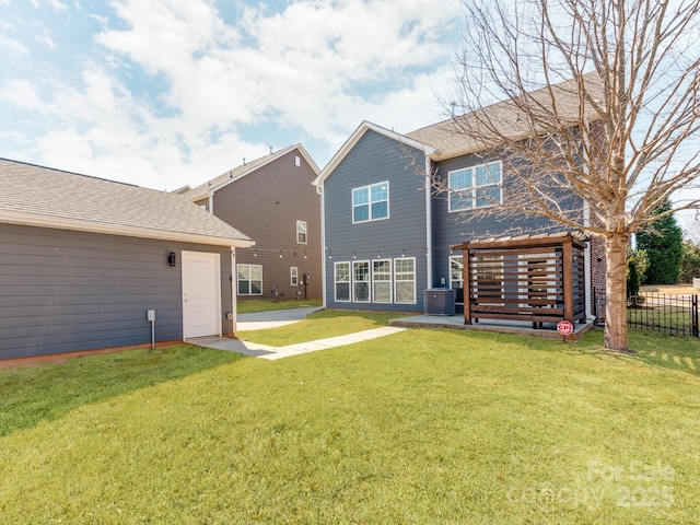 back of property with a lawn, roof with shingles, fence, a patio area, and central AC