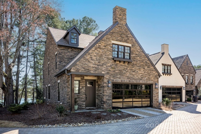 view of front of house featuring decorative driveway, a garage, stone siding, and a chimney