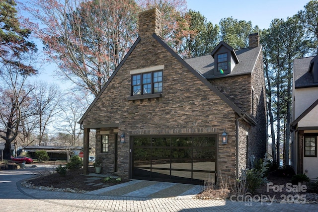 view of front facade with a garage, stone siding, driveway, and a chimney