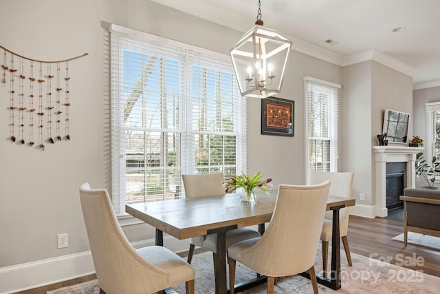 dining space featuring visible vents, ornamental molding, a glass covered fireplace, wood finished floors, and baseboards