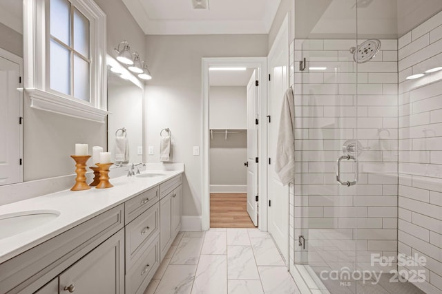 full bath featuring baseboards, double vanity, a stall shower, marble finish floor, and a sink