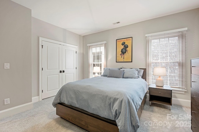 bedroom with a closet, visible vents, light colored carpet, and baseboards