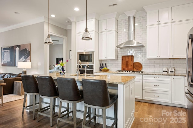 kitchen featuring visible vents, light wood finished floors, built in microwave, a sink, and wall chimney exhaust hood