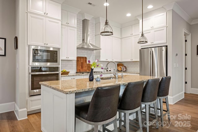 kitchen featuring visible vents, wall chimney range hood, light wood-style flooring, appliances with stainless steel finishes, and white cabinetry