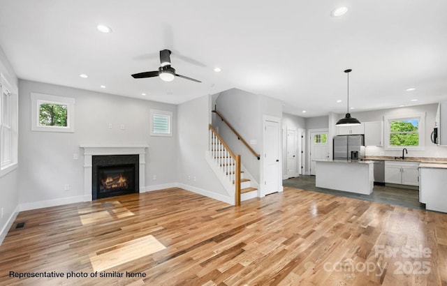 unfurnished living room featuring light wood-style flooring, stairway, a sink, and recessed lighting