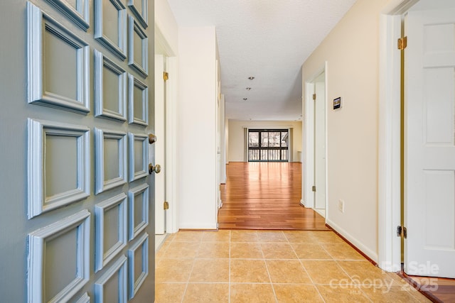 corridor with light tile patterned floors, a textured ceiling, and baseboards