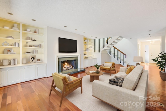 living area with built in shelves, stairway, light wood-style floors, a glass covered fireplace, and a textured ceiling