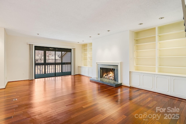 unfurnished living room featuring hardwood / wood-style floors, built in features, a warm lit fireplace, and a textured ceiling