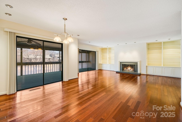 unfurnished living room with visible vents, built in shelves, a textured ceiling, and a glass covered fireplace