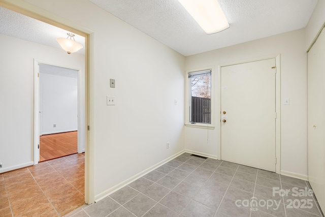 foyer with light tile patterned floors, visible vents, baseboards, and a textured ceiling