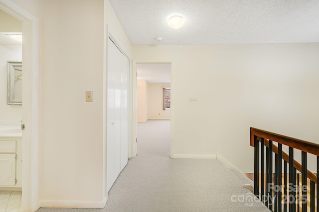 hallway with an upstairs landing, baseboards, carpet floors, and a textured ceiling