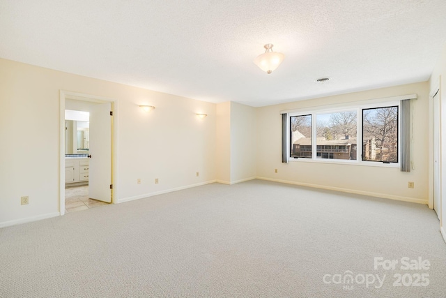 empty room with visible vents, light colored carpet, baseboards, and a textured ceiling