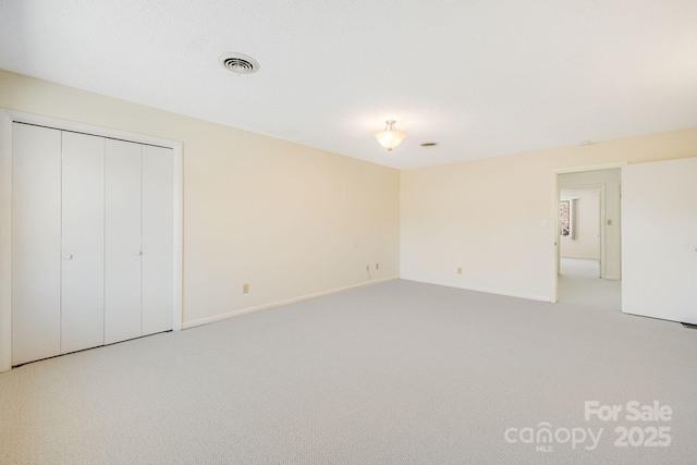 unfurnished bedroom featuring light carpet, visible vents, baseboards, and a closet