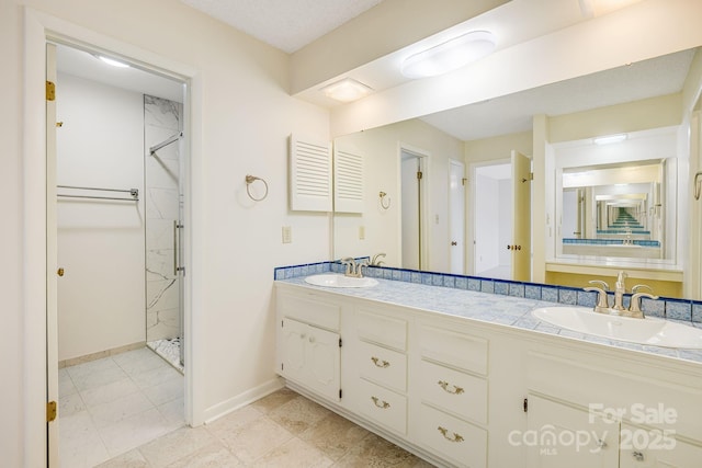 bathroom featuring double vanity, a shower stall, baseboards, and a sink