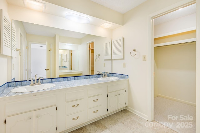 full bath featuring a closet, double vanity, baseboards, and a sink