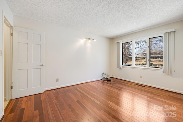 empty room with visible vents, baseboards, a textured ceiling, and hardwood / wood-style flooring