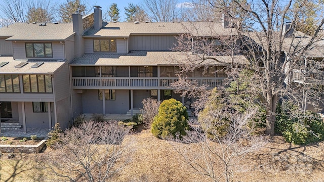 back of property featuring a patio, roof with shingles, a sunroom, and a chimney