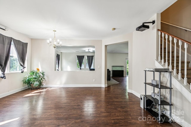 unfurnished room featuring a healthy amount of sunlight, an inviting chandelier, stairs, and wood finished floors