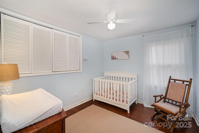 bedroom with dark wood-style floors, a ceiling fan, baseboards, and a nursery area