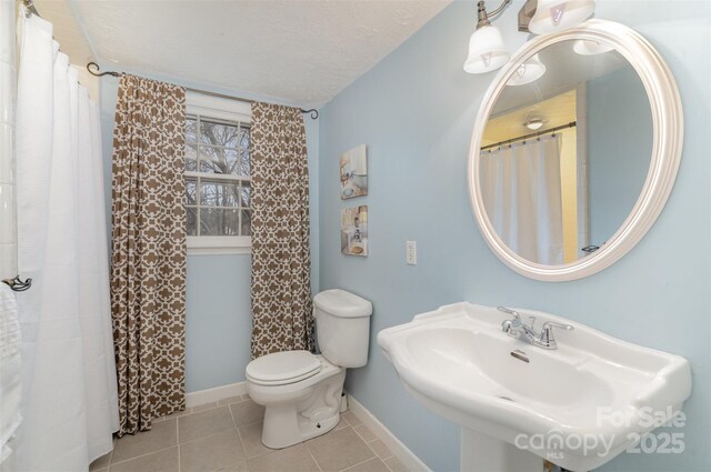 bathroom featuring baseboards, toilet, tile patterned flooring, a textured ceiling, and a sink