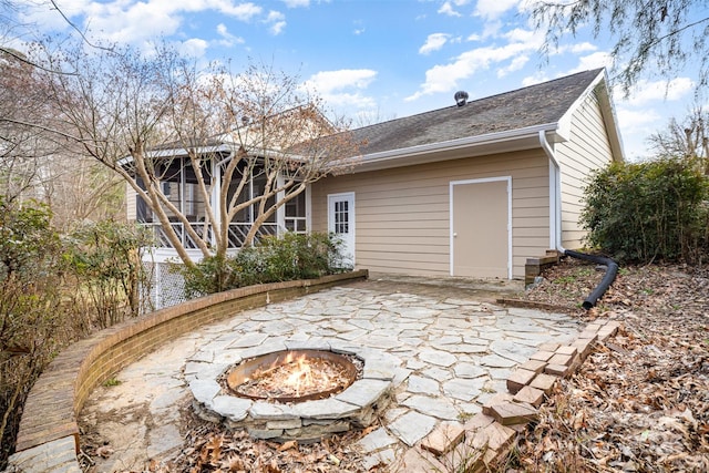 back of house with a shingled roof, a sunroom, a patio area, and a fire pit