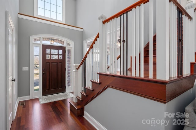 foyer entrance with a high ceiling, wood finished floors, visible vents, and baseboards