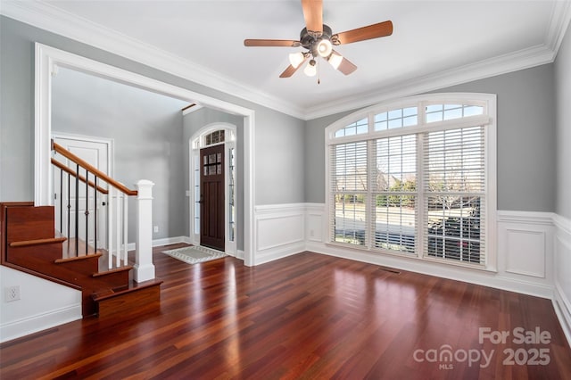 foyer with crown molding, stairway, wood finished floors, and a wainscoted wall