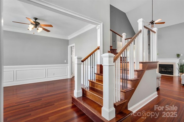 stairway with a fireplace with flush hearth, wood finished floors, a ceiling fan, and crown molding