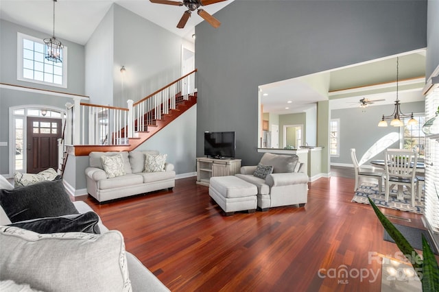 living room with wood finished floors, baseboards, a high ceiling, stairs, and ceiling fan with notable chandelier