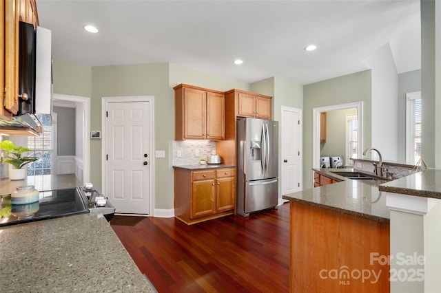 kitchen with stainless steel fridge with ice dispenser, dark stone counters, decorative backsplash, dark wood-style floors, and a sink