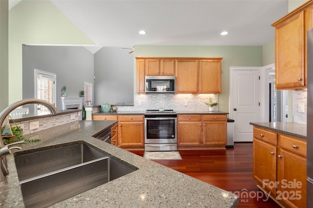 kitchen with tasteful backsplash, stainless steel appliances, dark stone counters, and a sink