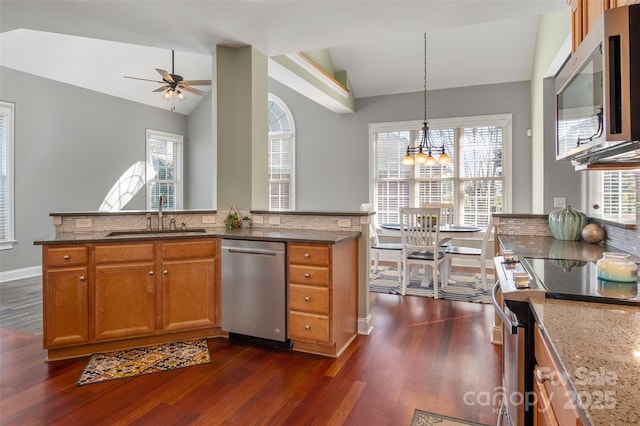 kitchen featuring a sink, dark stone counters, appliances with stainless steel finishes, brown cabinetry, and vaulted ceiling