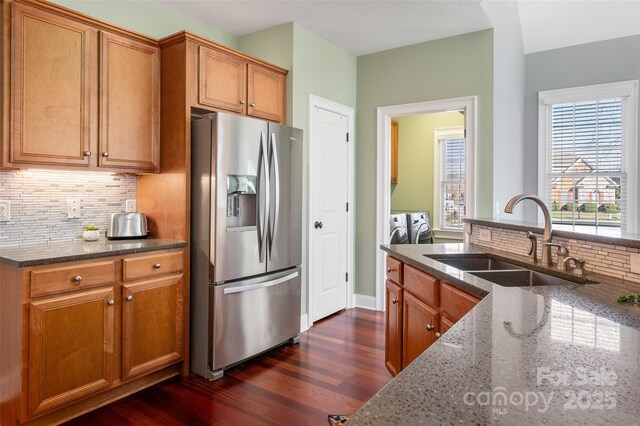 kitchen with washing machine and clothes dryer, a sink, dark stone counters, and stainless steel fridge with ice dispenser