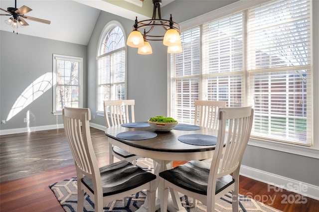 dining room featuring ceiling fan with notable chandelier, vaulted ceiling, wood finished floors, and baseboards